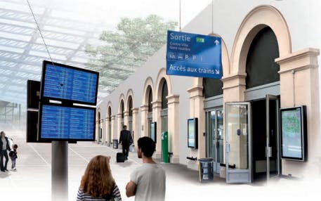 Voyageurs en gare regardant des écrans d'information