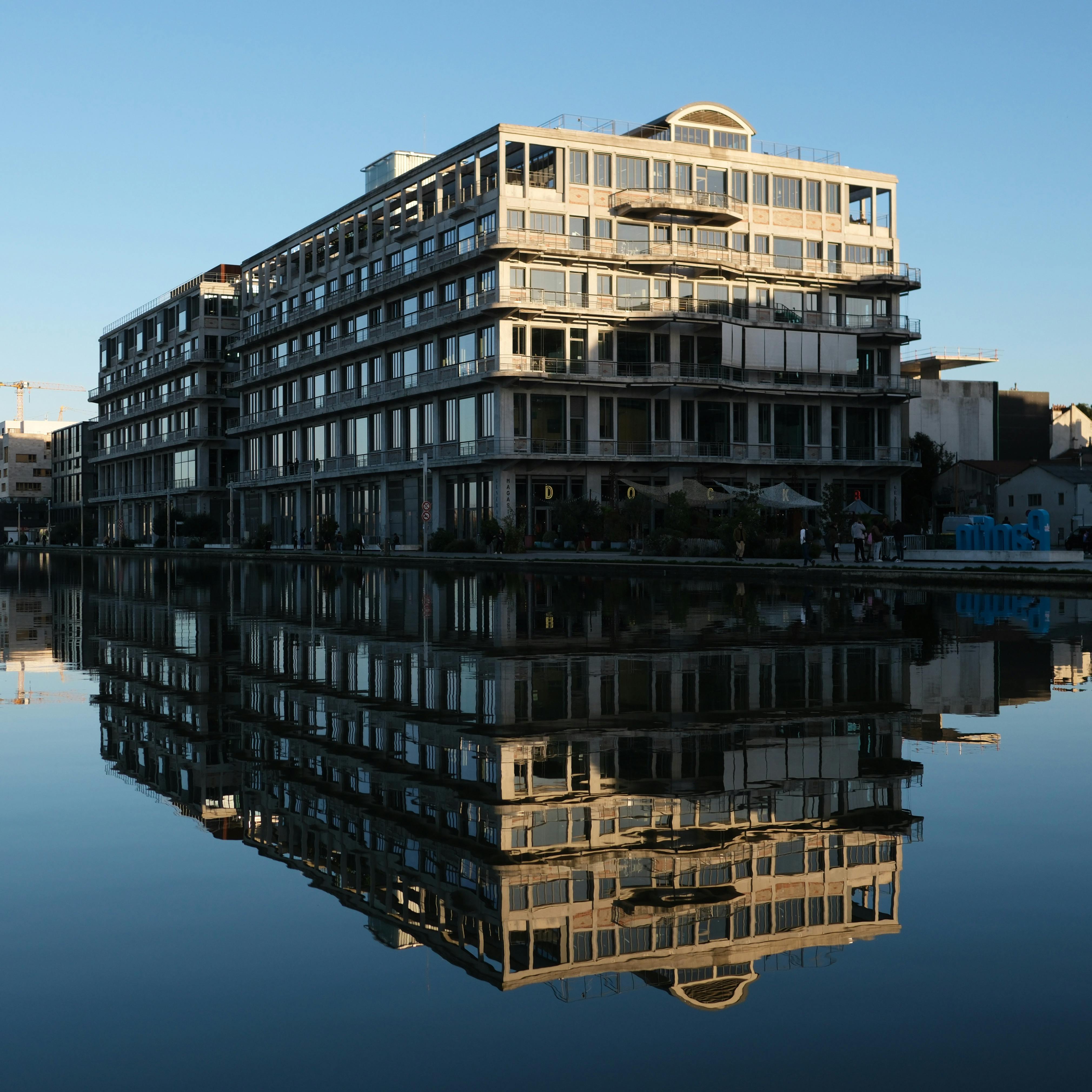 La facciata in cemento e metallo dei Magasins Généraux che si riflette nel Canal de l'Ourcq a Pantin